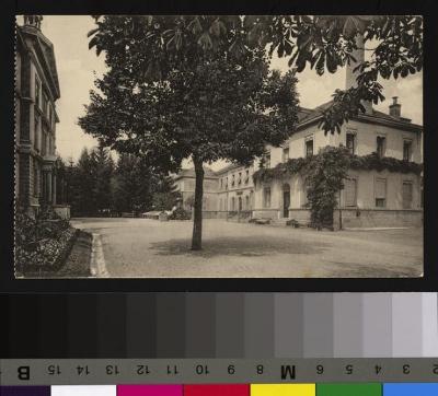 Vue sur l'entrée principale de l'Hôpital cantonal et du bâtiment où se trouvent les cuisines. Au fond de l'allée vers les arbres, une voiture. A l'angle droit de l'image, la cheminée des cuisines est cachée par les arbres.